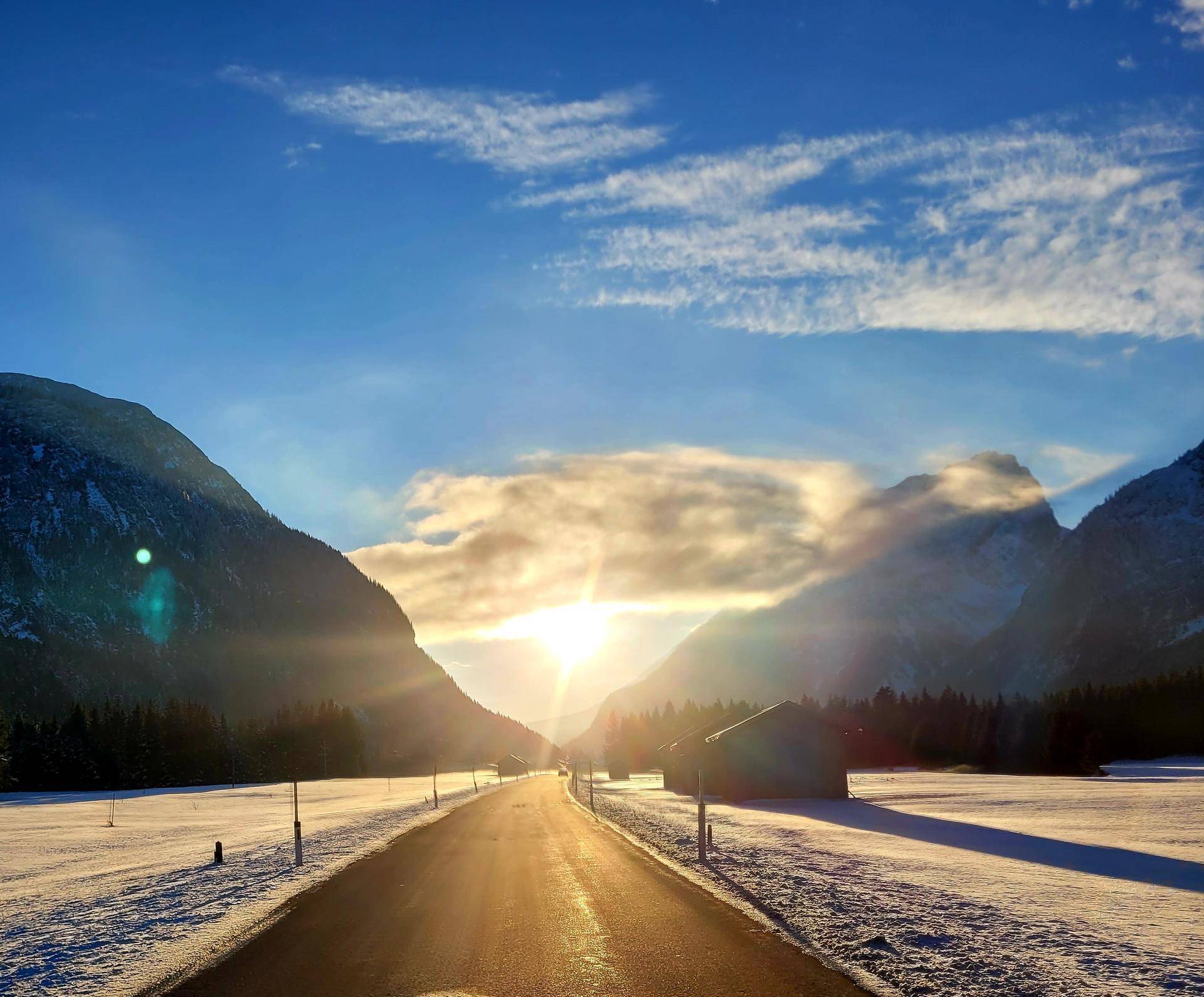 Sonniger Wintertag in einem verschneiten Tal mit einer Straße, die in die Berglandschaft führt.