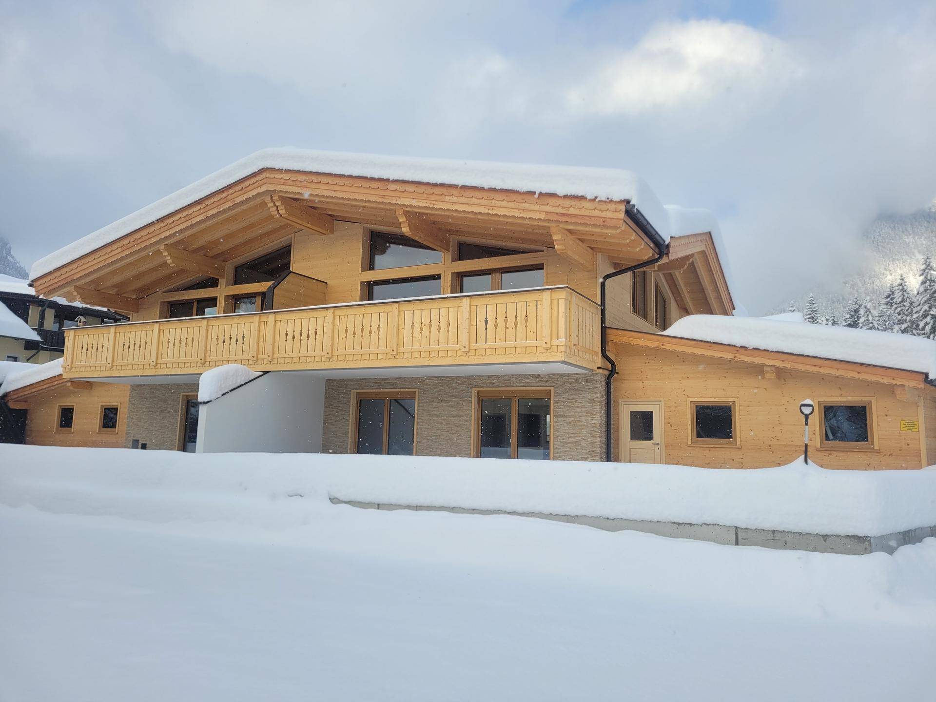 Modernes Holzhaus im Chalet-Stil mit Balkon und verschneitem Dach in alpiner Landschaft.