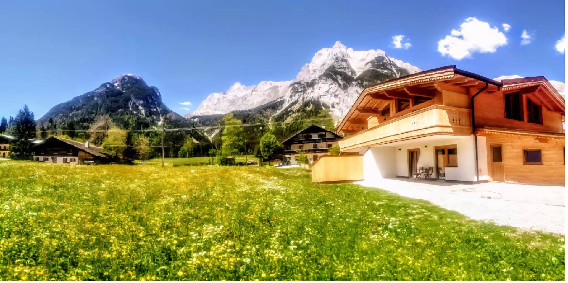 Panoramablick auf ein Chalet-Haus mit blühender Wiese im Vordergrund und majestätischen, schneebedeckten Bergen.