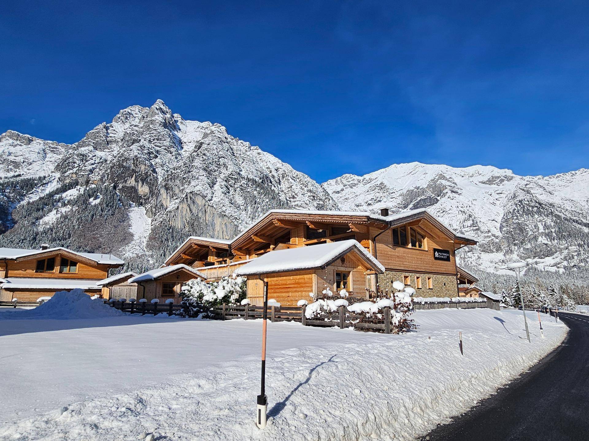 Gruppe von Holzhäusern in einer weiten, schneebedeckten Landschaft mit majestätischen Bergen.