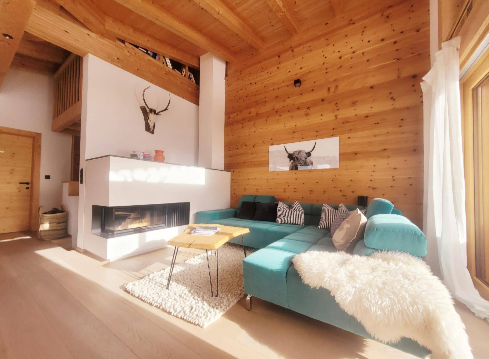 Helles Wohnzimmer im alpinen Stil mit Holzwänden, Kamin und türkisfarbenem Sofa.