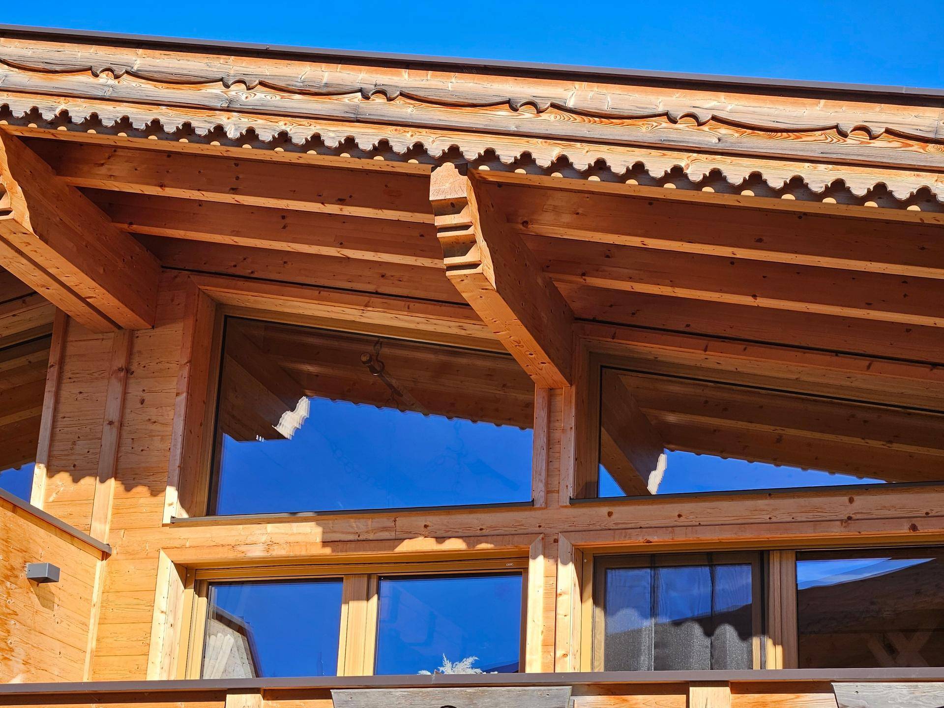 Detailansicht einer Holzfassade mit kunstvollen Schnitzereien und großen Fenstern.