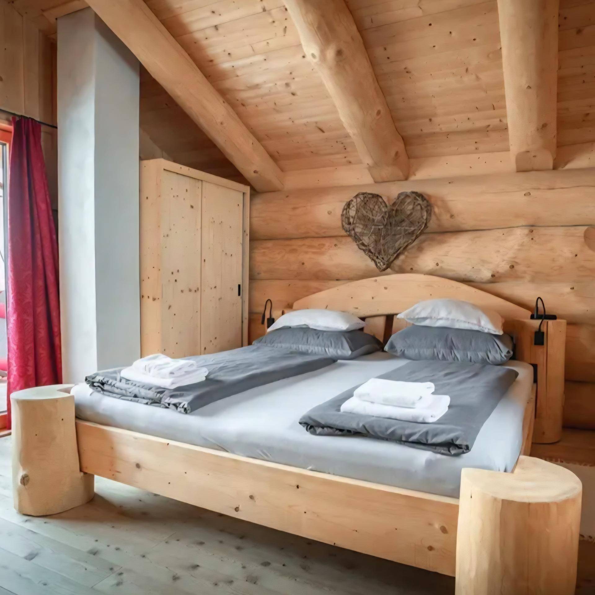Gemütliches Schlafzimmer im Blockhausstil mit sichtbaren Holzbalken und rustikalem Doppelbett.