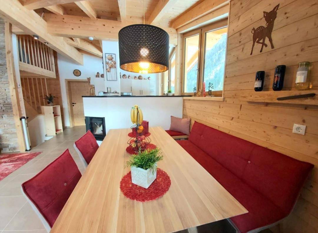 Rustikaler Essbereich mit Holzwänden, roter Sitzbank und Blick auf die verschneite Landschaft.