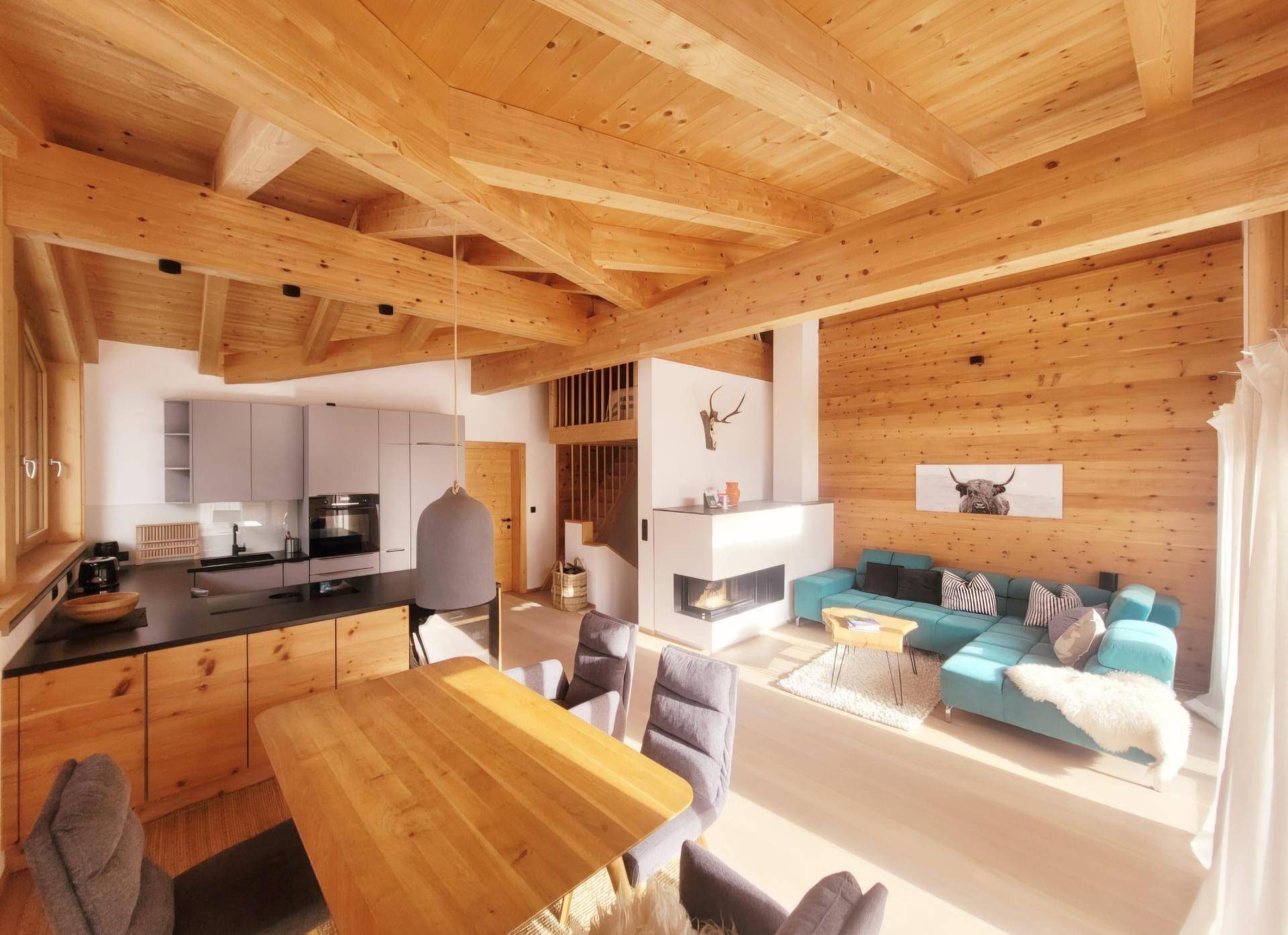 Offener Wohn-Essbereich mit integrierter Küche, Holzbalkendecke und modernem Kamin.