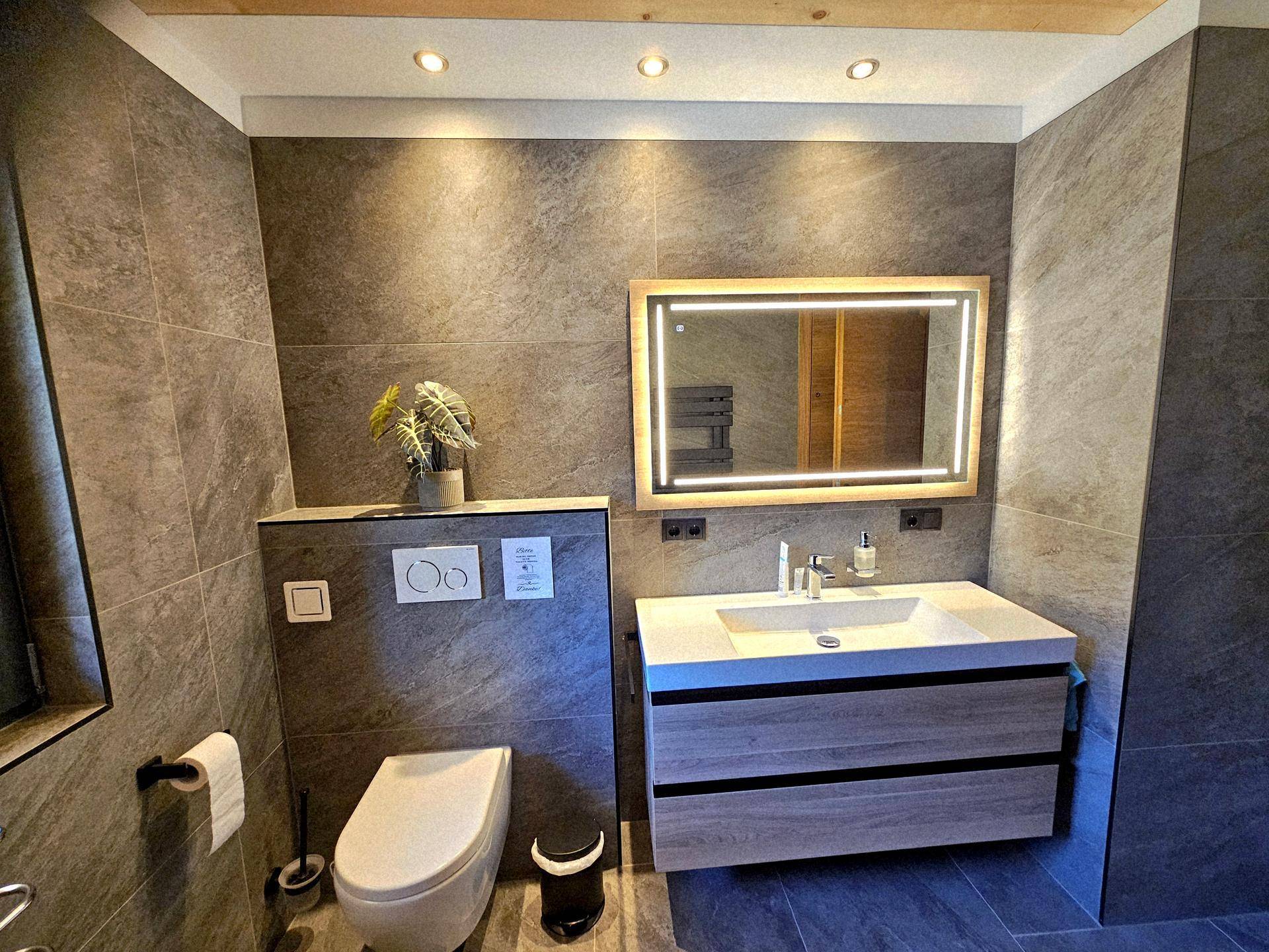 Modernes Badezimmer mit grauen Fliesen, schwebendem Waschtisch und wandhängendem WC.
