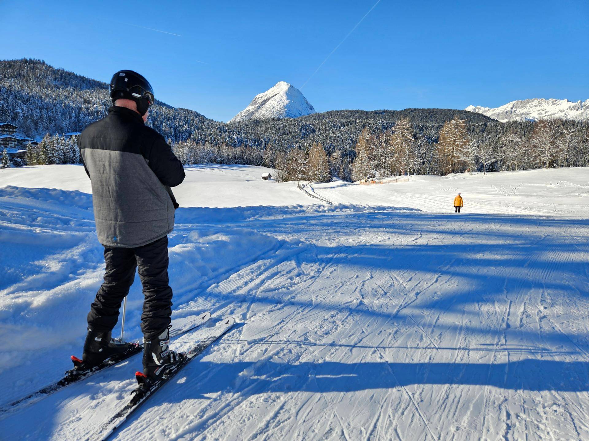 Skifahrer blickt auf eine weite, verschneite Berglandschaft unter strahlend blauem Himmel.