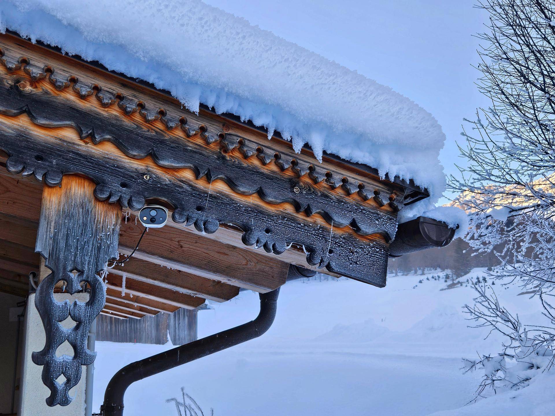 Detailansicht eines traditionellen Holzdaches mit Schnee und einer Überwachungskamera.