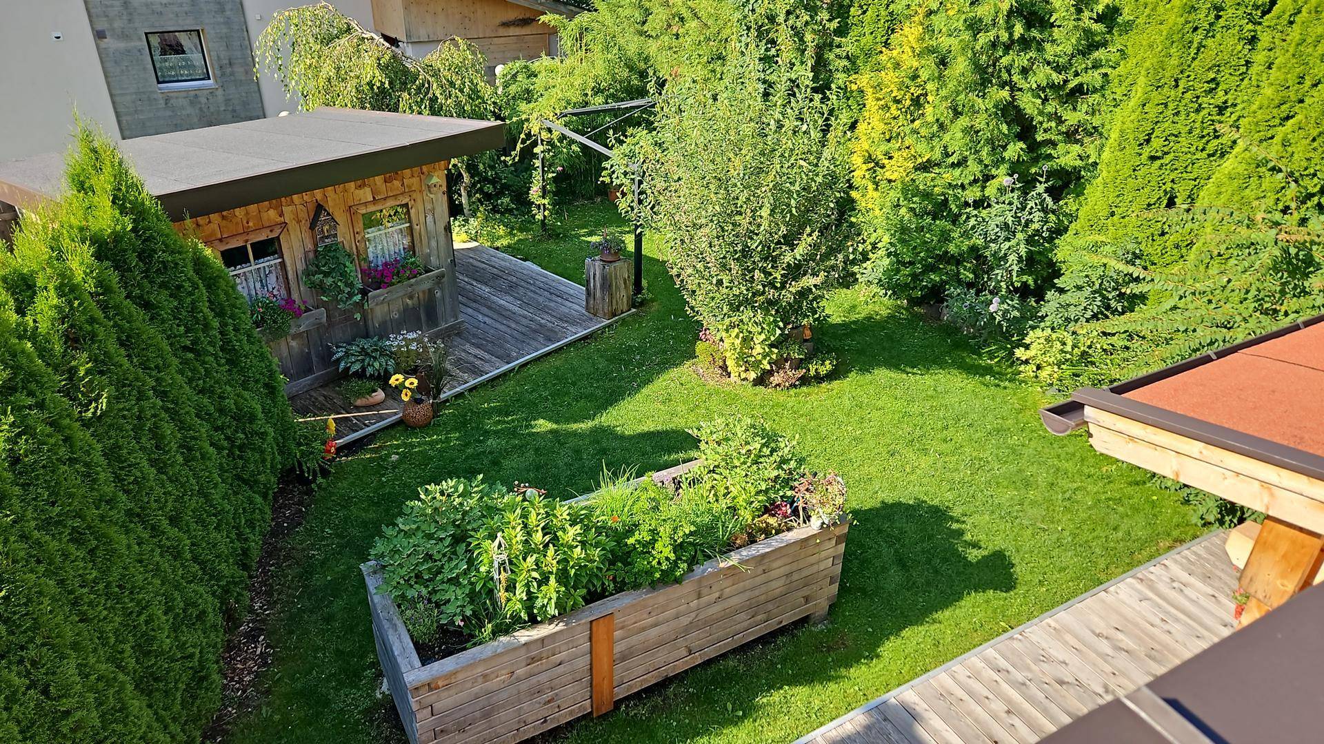 Gepflegter Garten mit Rasenfläche, Hochbeet und einem kleinen Holzhaus umgeben von Hecken.