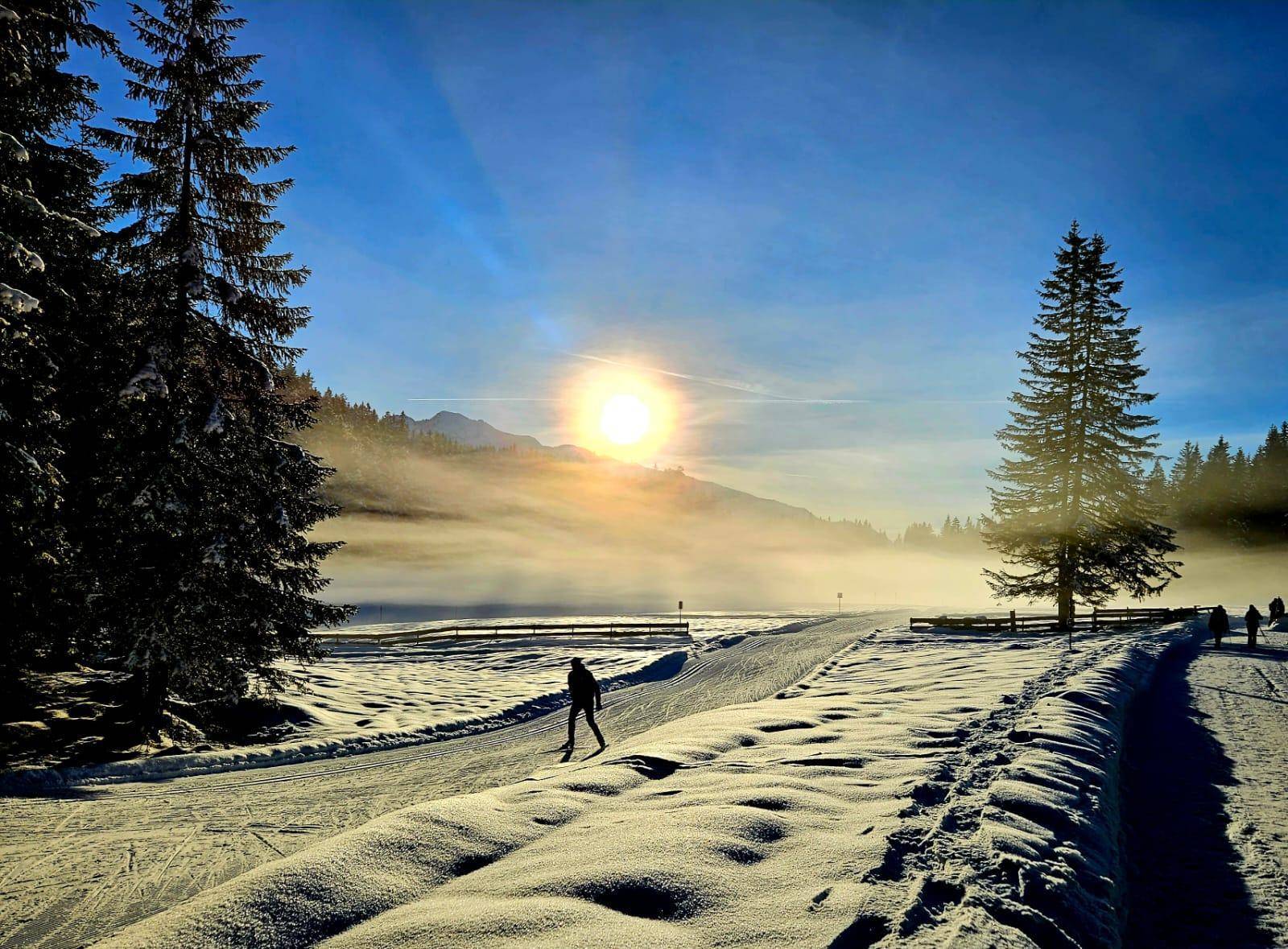 Sonniger Wintertag in den Bergen mit Langläufer auf verschneiter Loipe und Nebelstimmung.