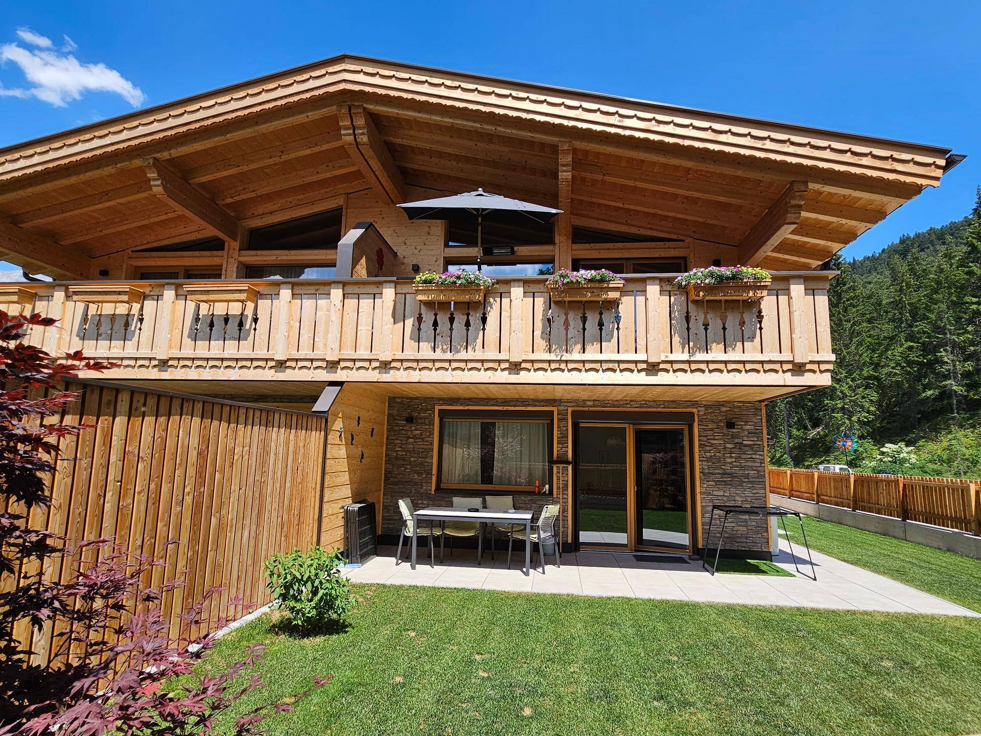 Chalet-Stil Haus mit gepflegtem Rasen und einer möblierten Terrasse im Freien.