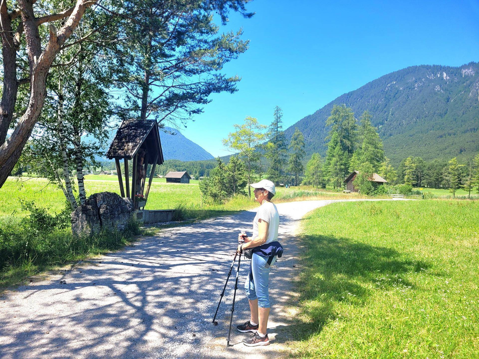 Wanderin auf einem Feldweg in einer grünen Berglandschaft unter strahlend blauem Himmel.