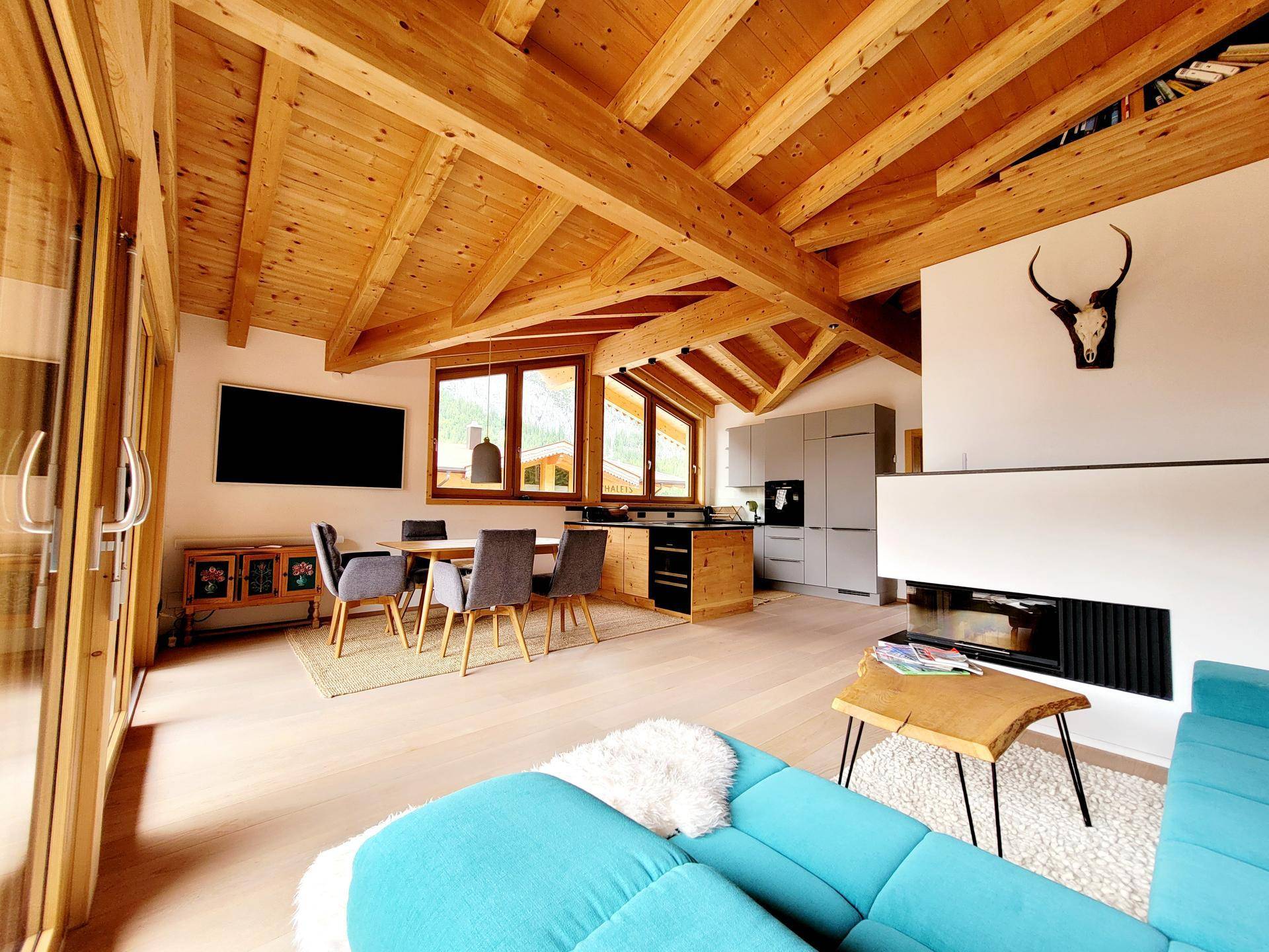 Heller Wohn-Essbereich mit sichtbaren Holzbalken, modernem Kamin und gemütlichem Sofa.