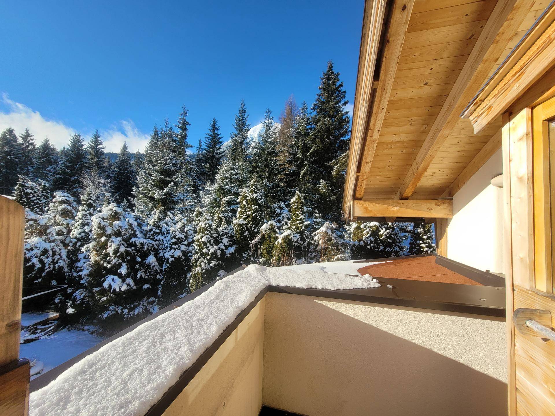 Verschneiter Balkon mit Blick auf die umliegenden schneebedeckten Tannenbäume und Berge.
