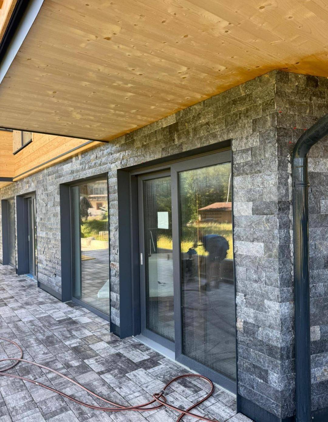 Detailansicht einer modernen Fassade mit Natursteinverkleidung und großen Glasschiebetüren.