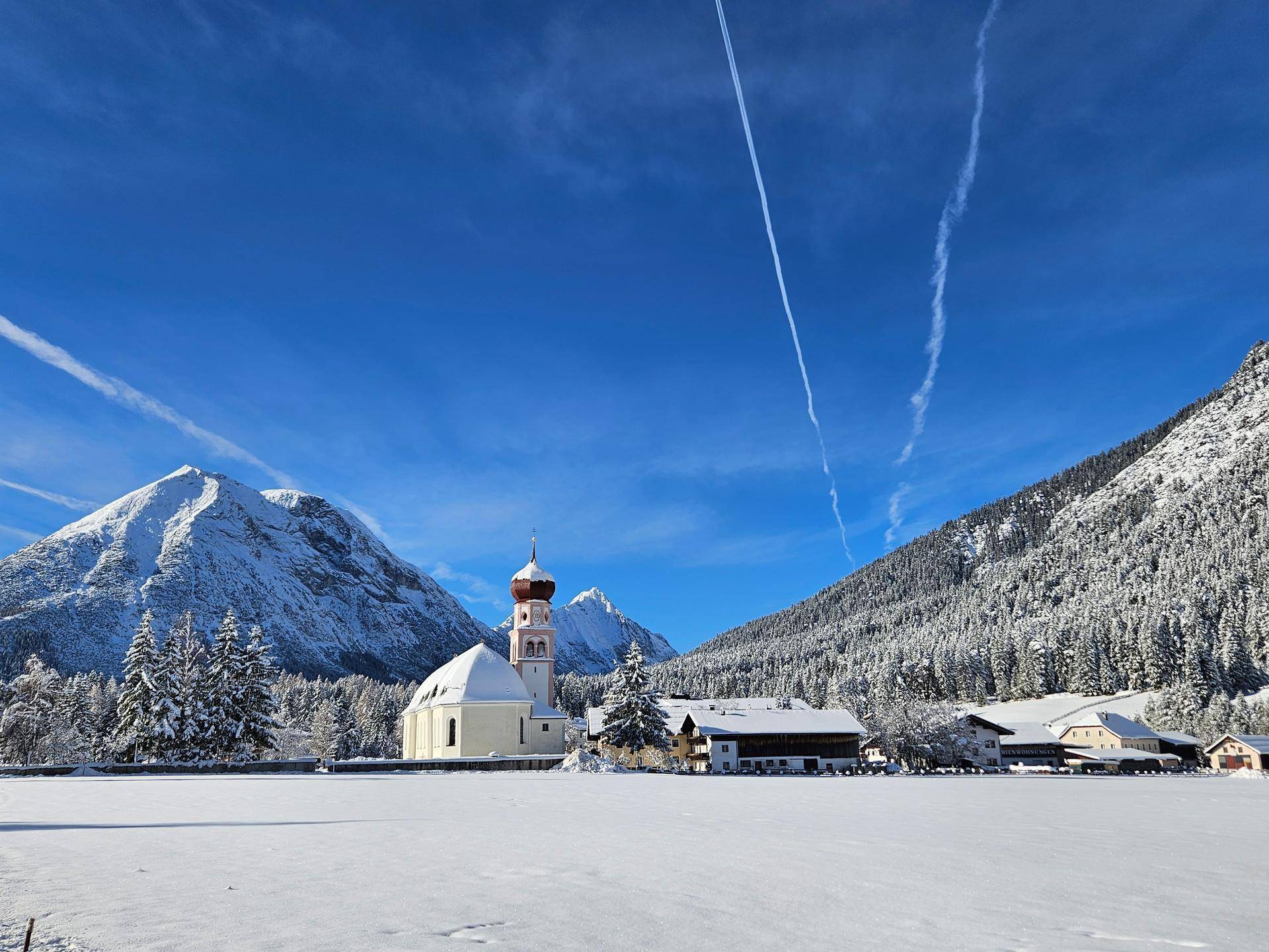 Ein malerisches Dorf mit einer Kirche in einem verschneiten Tal, umgeben von imposanten Bergen.