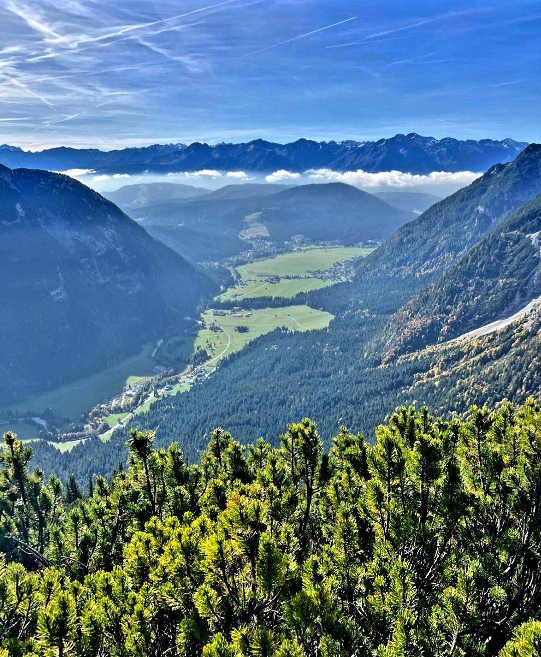 Eine weite grüne Talansicht, umgeben von majestätischen Bergen, mit verstreuten Häusern und Wäldern.