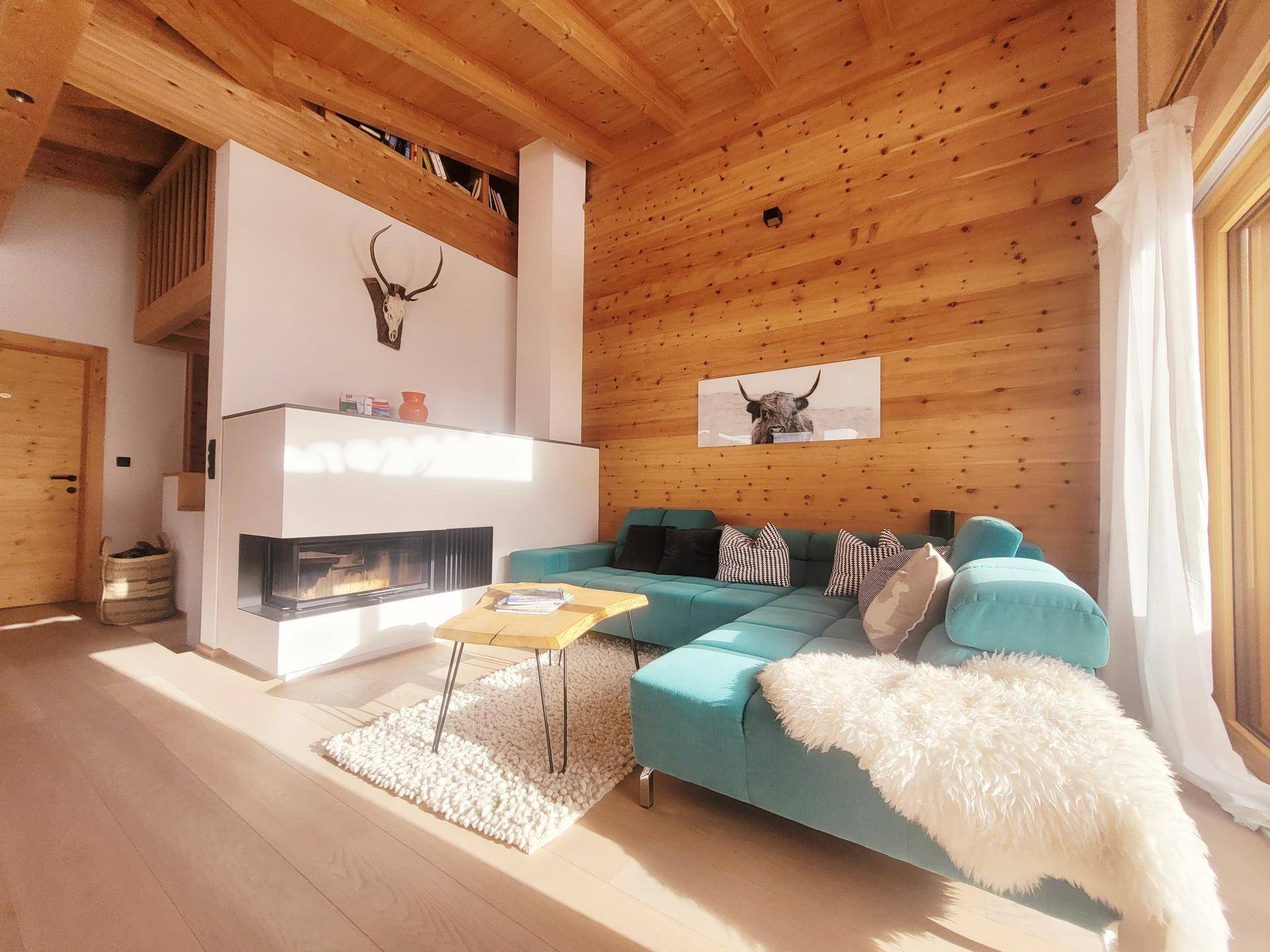 Gemütliches Wohnzimmer mit türkisfarbenem Sofa, modernem Kamin und Holzwänden.