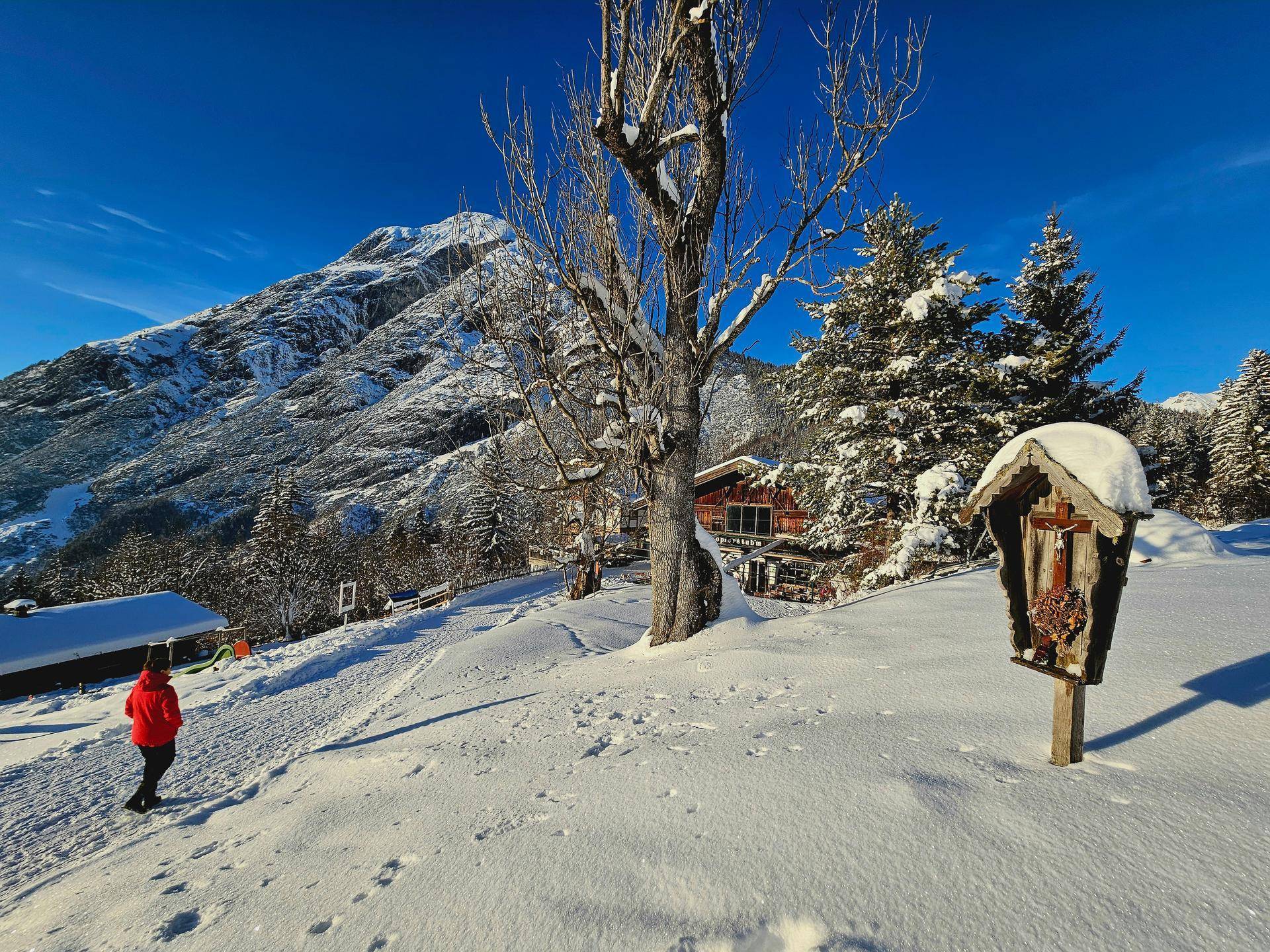 Winterliche Berglandschaft mit einer Person auf einem verschneiten Weg und einem kleinen Schrein.