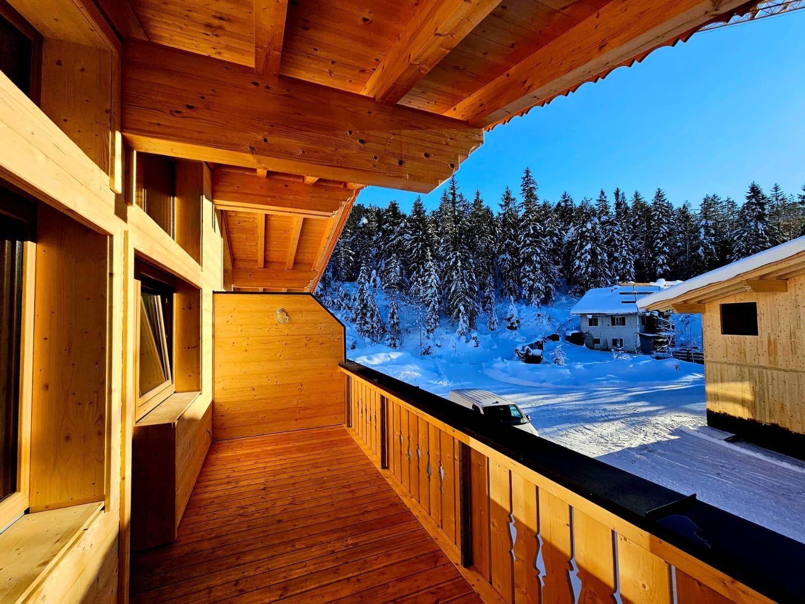 Heller Holz-Balkon mit Blick auf verschneite Bäume und die umliegende Winterlandschaft.