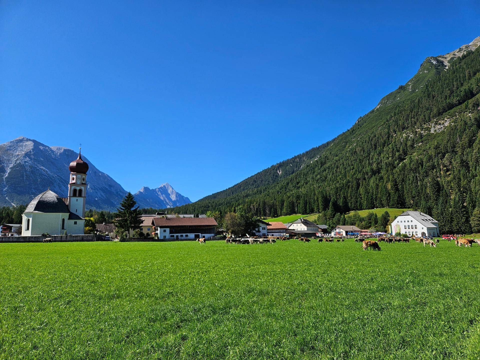 Idyllische Landschaft mit grünen Wiesen, einer Kirche, Häusern und majestätischen Bergen im Hintergrund.