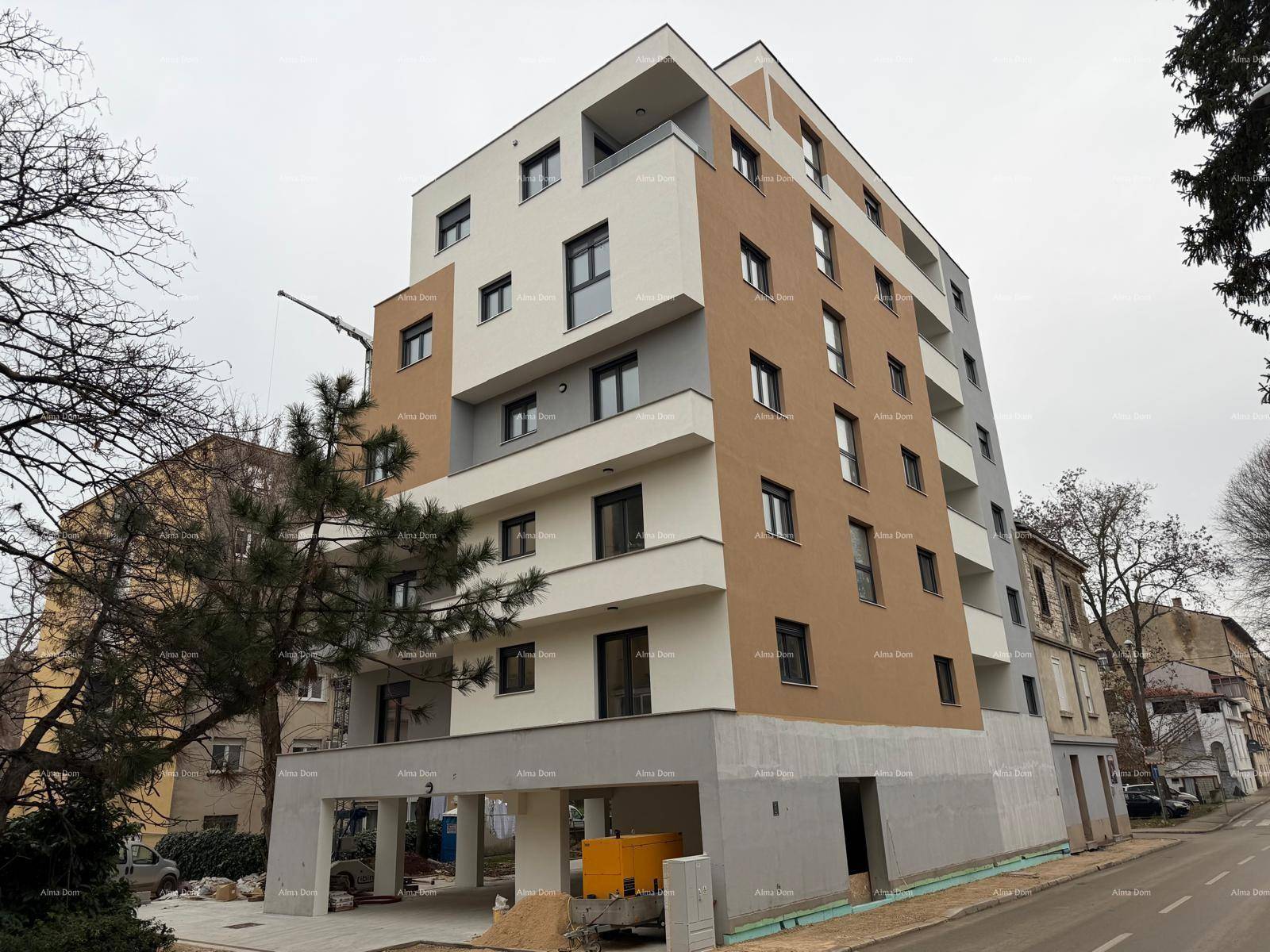 Ansicht des modernen Neubaus mit mehrfarbiger Fassade und Balkonen, umgeben von Bäumen.