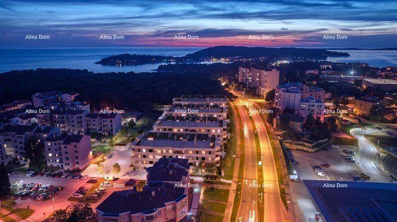 Nächtliche Luftaufnahme einer beleuchteten Küstenstadt mit Gebäuden und Straßen am Meer.
