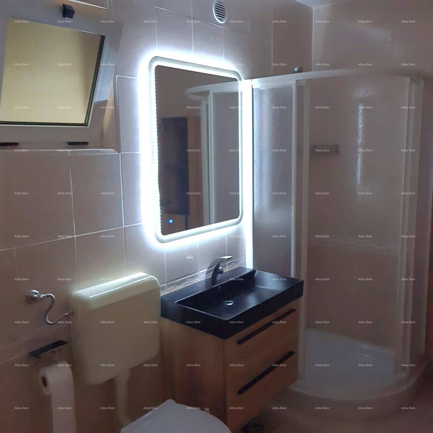 Modernes Badezimmer mit Duschkabine, beleuchtetem Spiegel und dunklem Waschbeckenunterschrank.