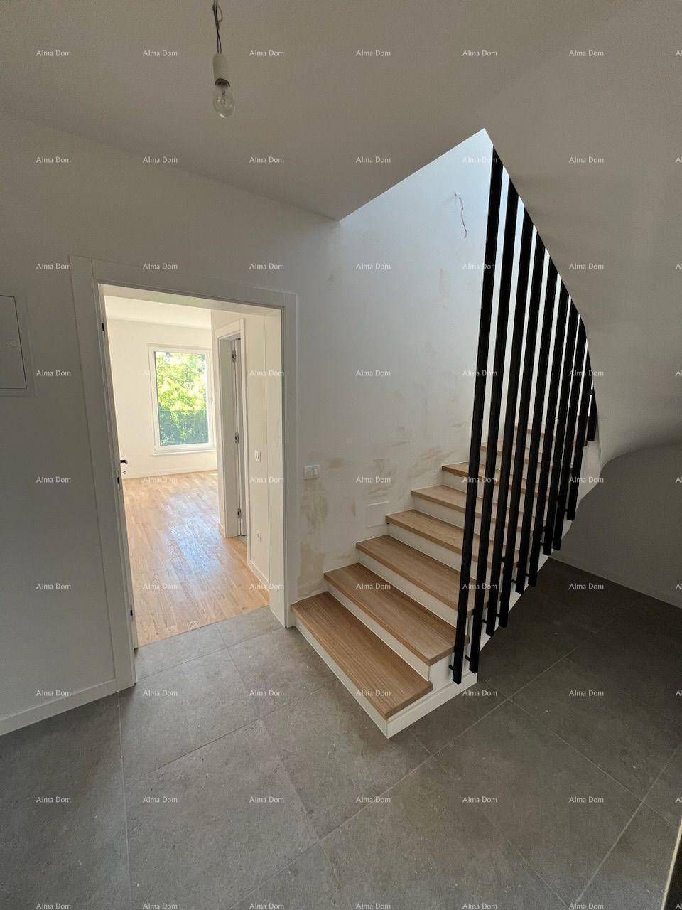 Eingangsbereich mit moderner Holztreppe und dunklem Fliesenboden, der zu einem weiteren Raum führt.