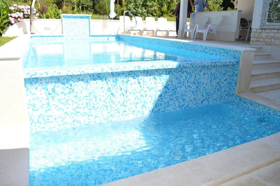 Detailansicht des Pools mit blauen Mosaikfliesen und einem eleganten Wasserfall.