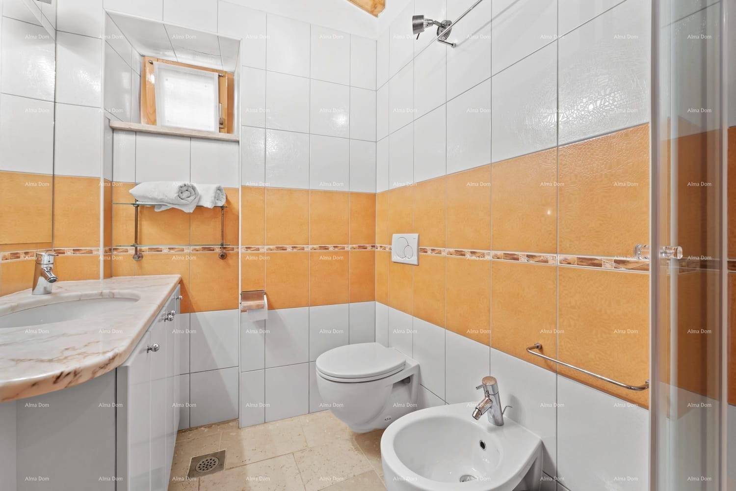 Badezimmer mit WC, Bidet, Waschtisch und orange-weißen Wandfliesen sowie Duschbereich.