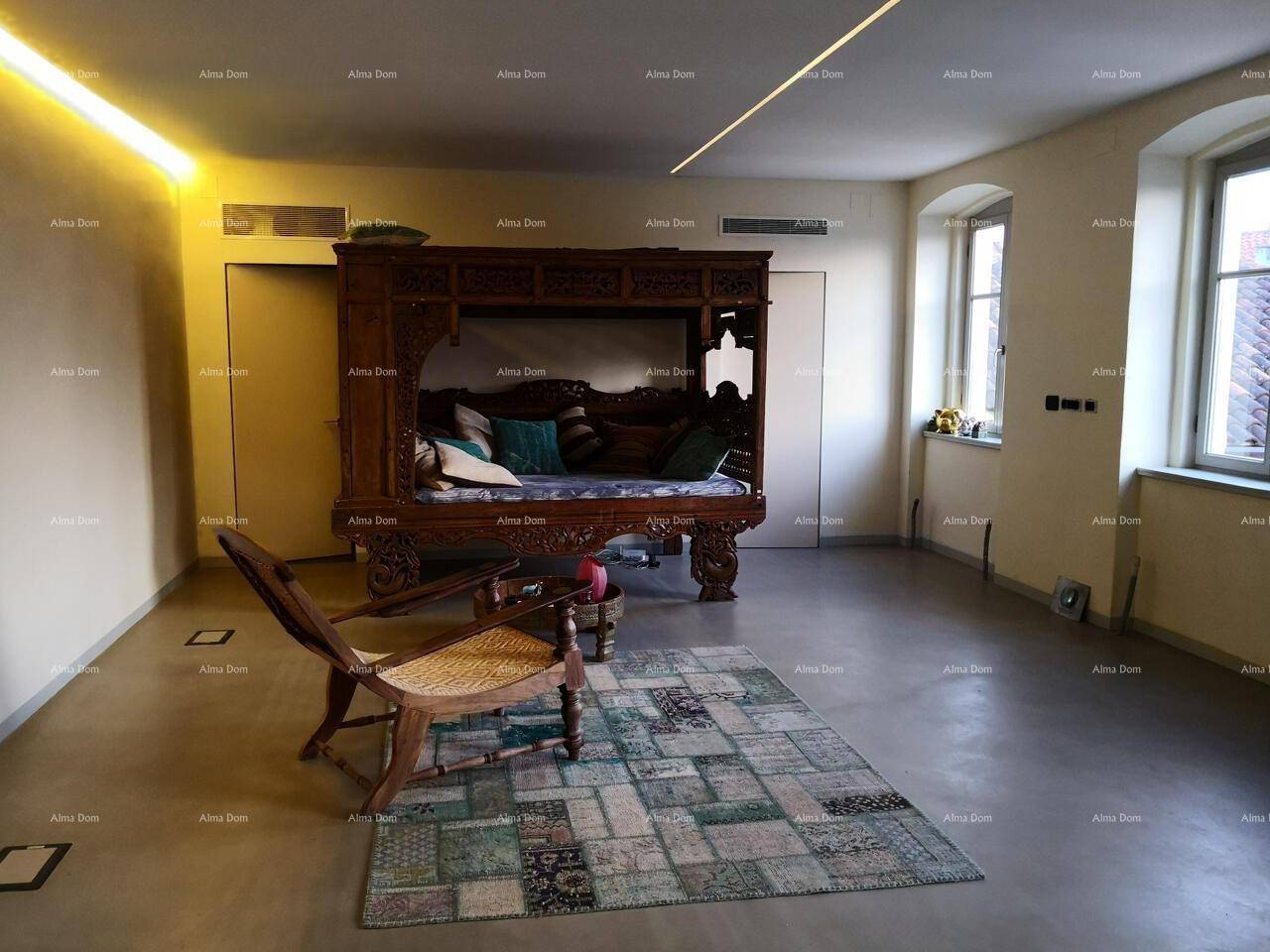 Schlafzimmer mit einem kunstvoll geschnitzten Holzbett, Patchwork-Teppich und großen Fenstern.
