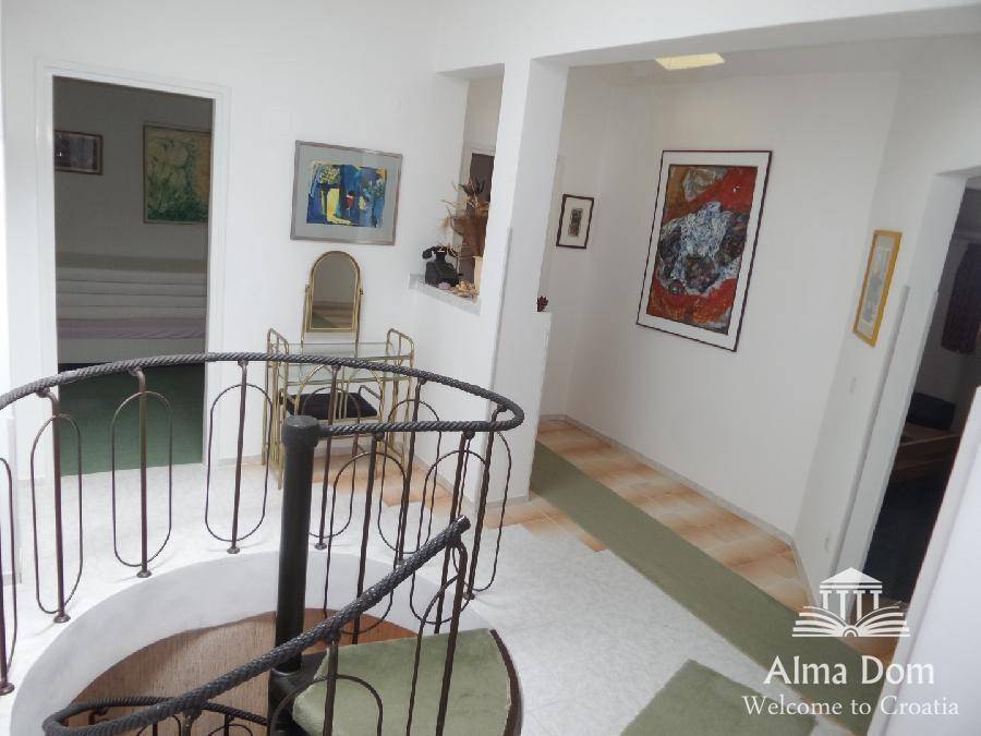 Heller Flur mit Wendeltreppe, Kunstwerken an den Wänden und Teppichläufern, offen gestaltet.