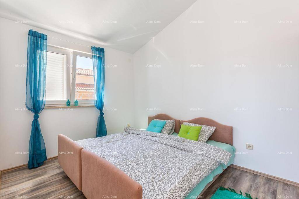 Helles Schlafzimmer mit Doppelbett, farbenfrohen Kissen und blauen Vorhängen am Fenster.