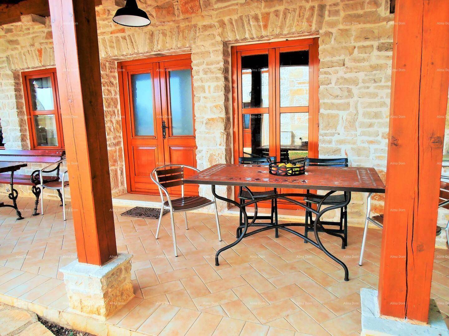 Überdachte Terrasse mit Holzbalken und Essbereich im Freien vor dem Steinhaus.