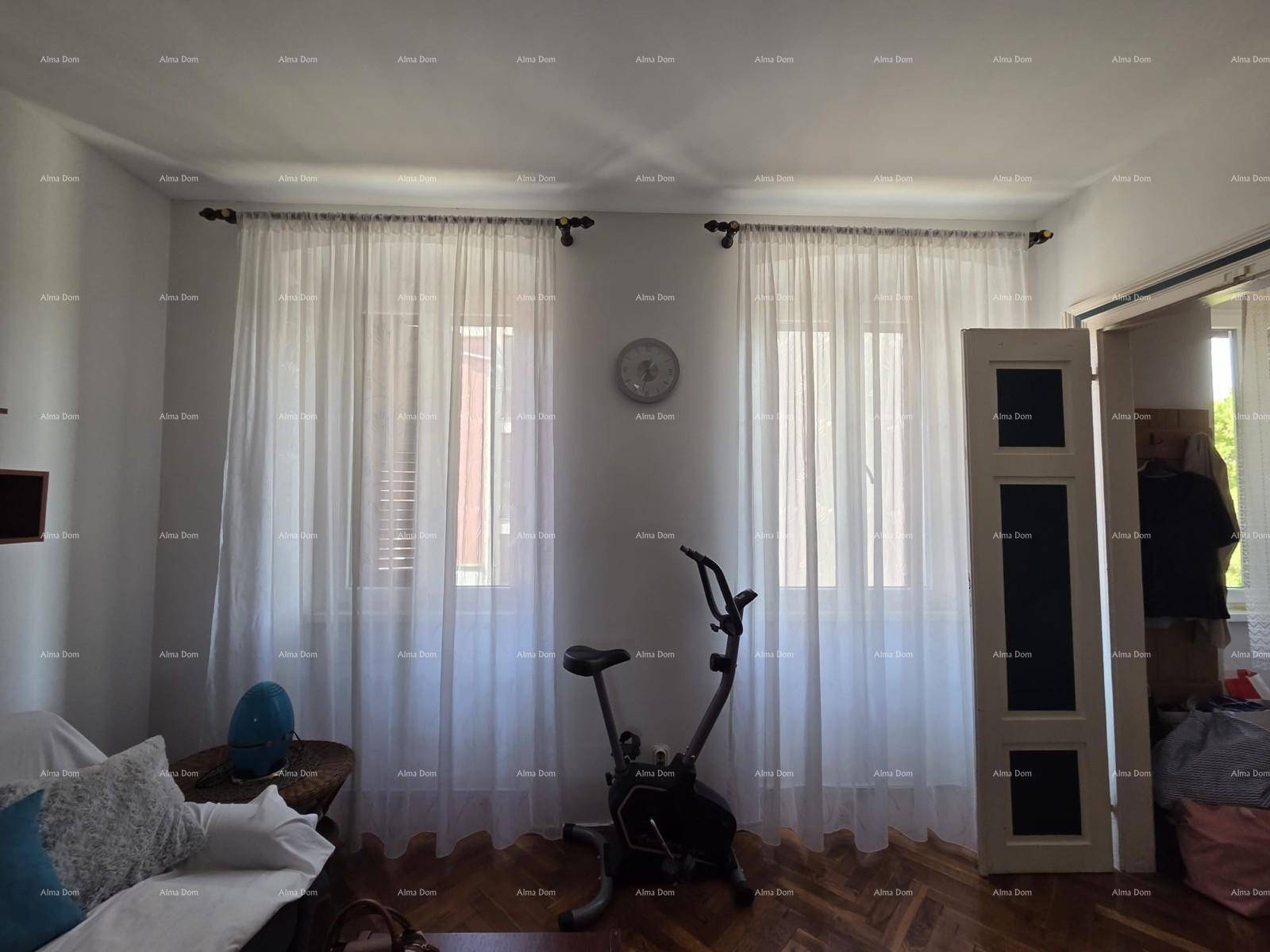 Zwei Fenster im Wohnzimmer mit hellen Vorhängen und einem Heimtrainer.