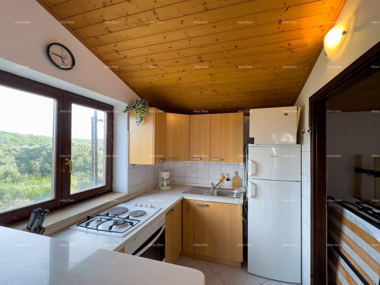 Kompakte Küche mit Holzfronten, Gasherd, Kühlschrank und einem Fenster mit weitem Blick.