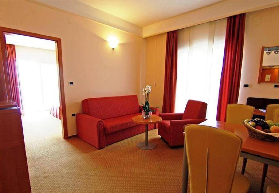 Wohnbereich mit rotem Sofa, Sessel, Esstisch und Teppichboden, verbunden durch einen eleganten Bogen.