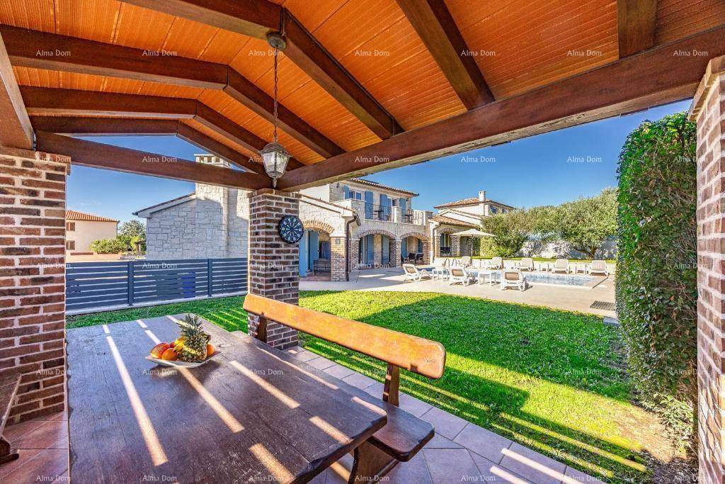 Überdachte Terrasse mit Holztisch und Bänken, Blick auf den Pool und Gartenbereich.