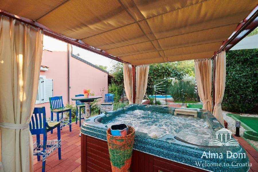 Geräumiger Terrassenbereich mit Whirlpool, Sitzgelegenheiten und Blick auf den Pool im Hintergrund.