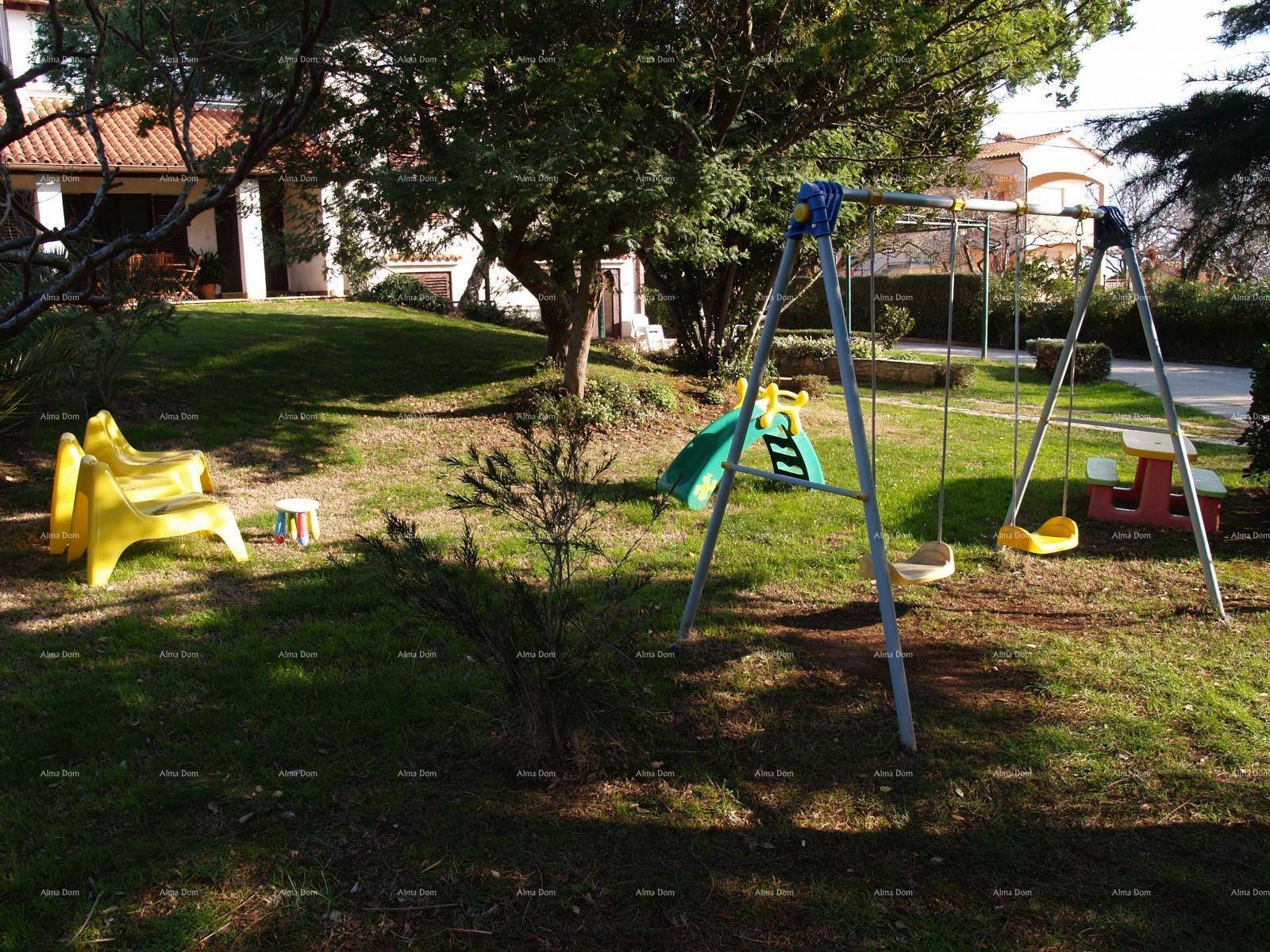 Grüner Gartenbereich mit Kinderspielplatz, Schaukeln und Rutsche unter Bäumen.
