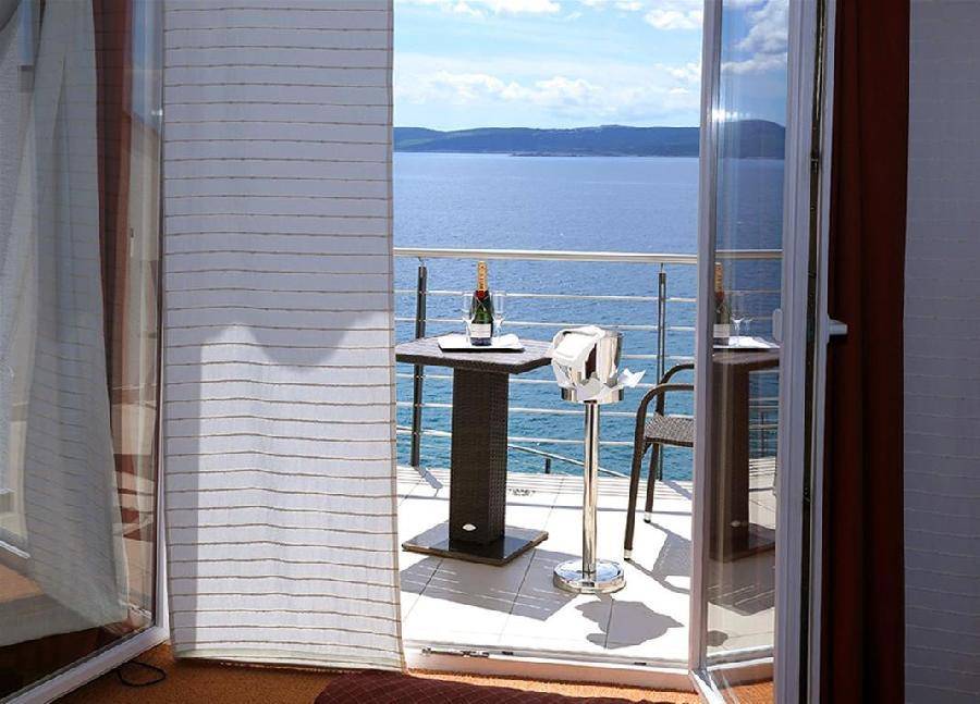 Balkon mit einem Tisch, Champagnerkübel und weitem Meerblick, zugänglich durch eine Glastür.