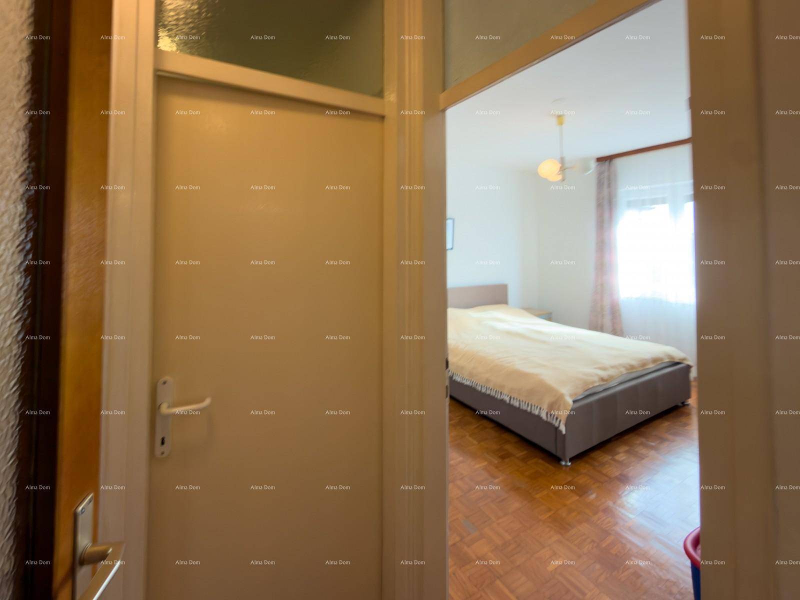 Schlafzimmer mit Doppelbett und Parkettboden, sichtbar durch eine offene Tür.
