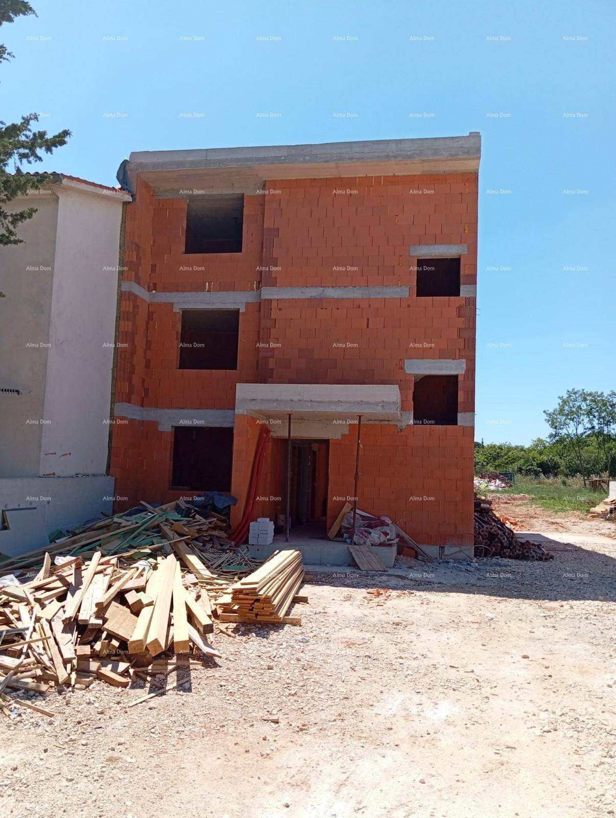 Frontansicht des Rohbaus eines Mehrfamilienhauses mit sichtbaren Ziegelwänden und Baumaterialien.
