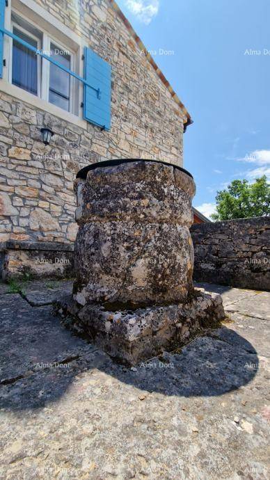 Alter steinerner Brunnen vor der Fassade des traditionellen Steinhauses unter strahlendem Himmel.