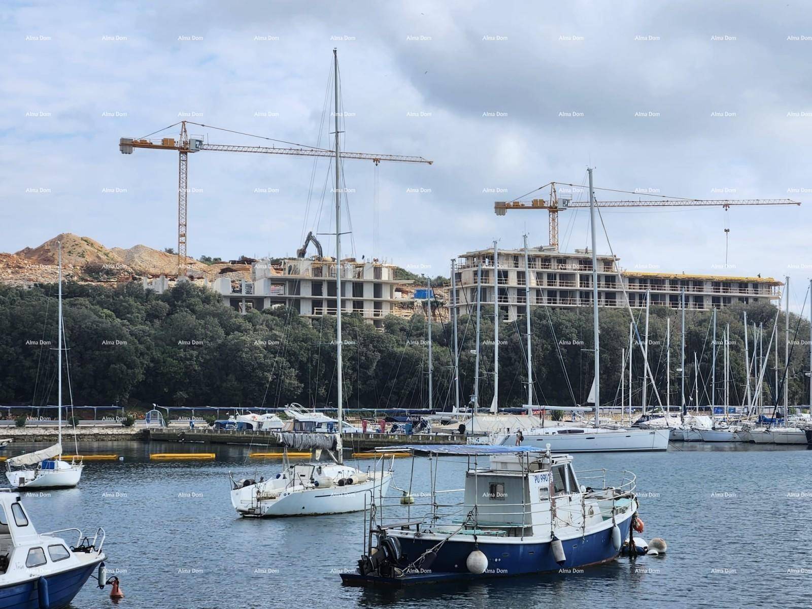 Boote im Yachthafen mit Kränen und im Bau befindlichen Gebäuden am bewaldeten Ufer.