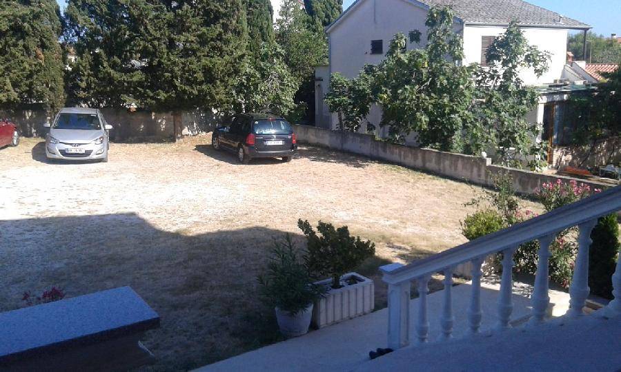 Ein offener Parkplatz mit zwei Autos, umgeben von Bäumen und einer niedrigen Mauer.