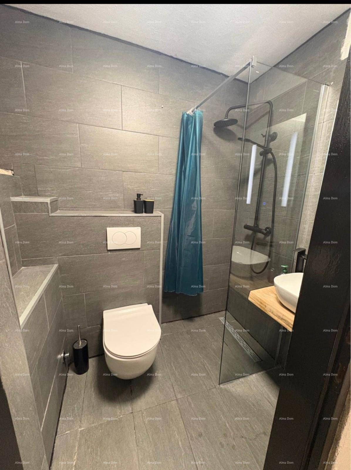 Modernes Badezimmer mit grauen Fliesen, wandhängendem WC und begehbarer Dusche mit Glaswand.