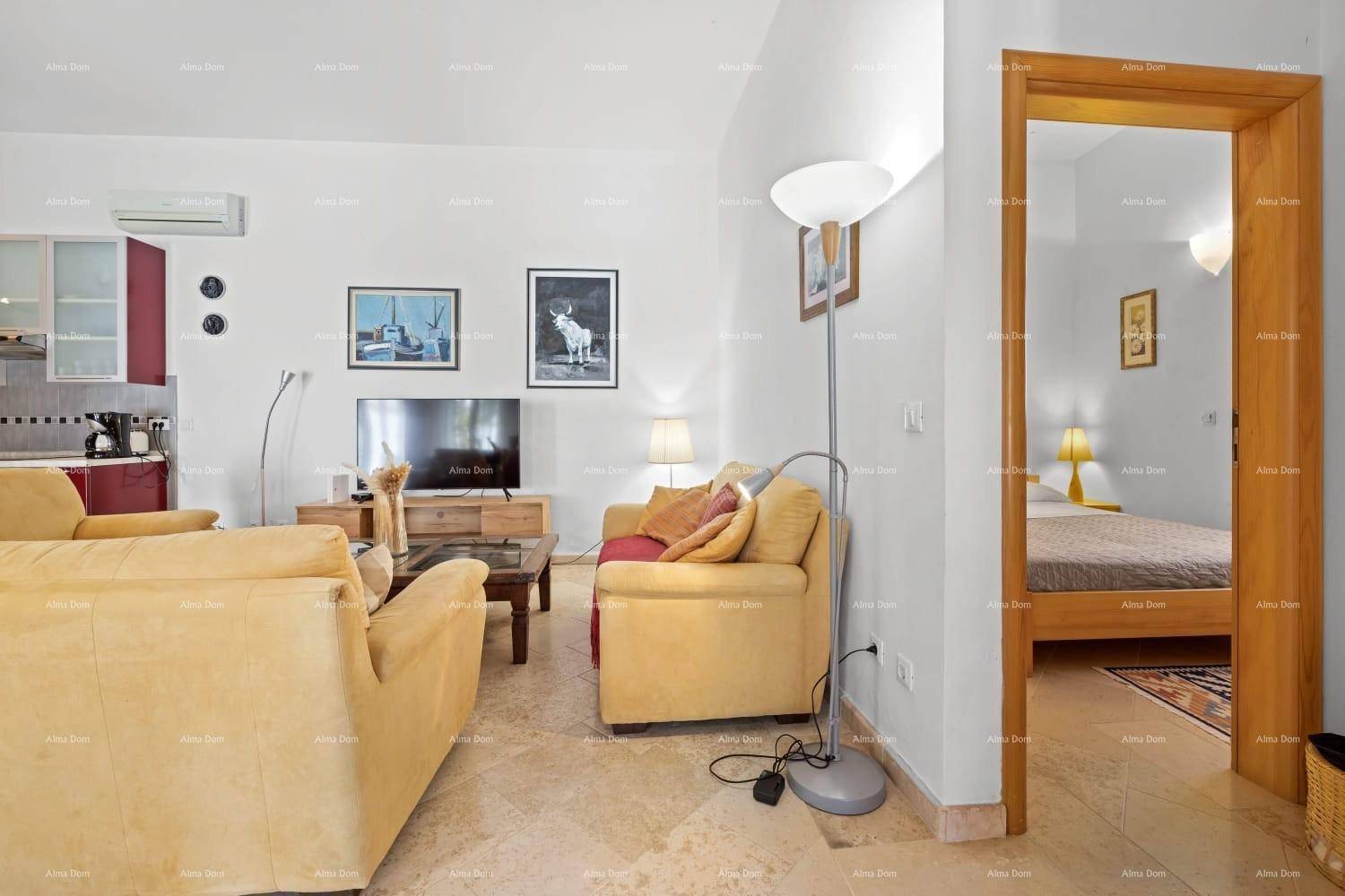 Wohnbereich mit beigen Sofas, Fliesenboden und offenem Zugang zu einem angrenzenden Schlafzimmer.
