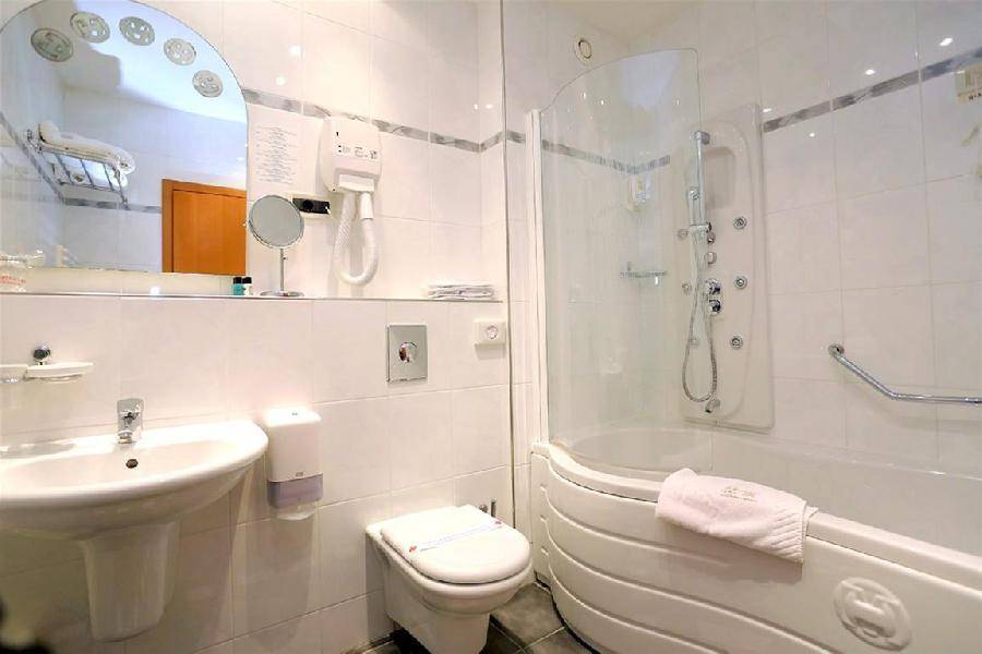 Helles Badezimmer mit Duschkabine, WC, Waschbecken und weißen Fliesen, ausgestattet mit Haltegriffen.